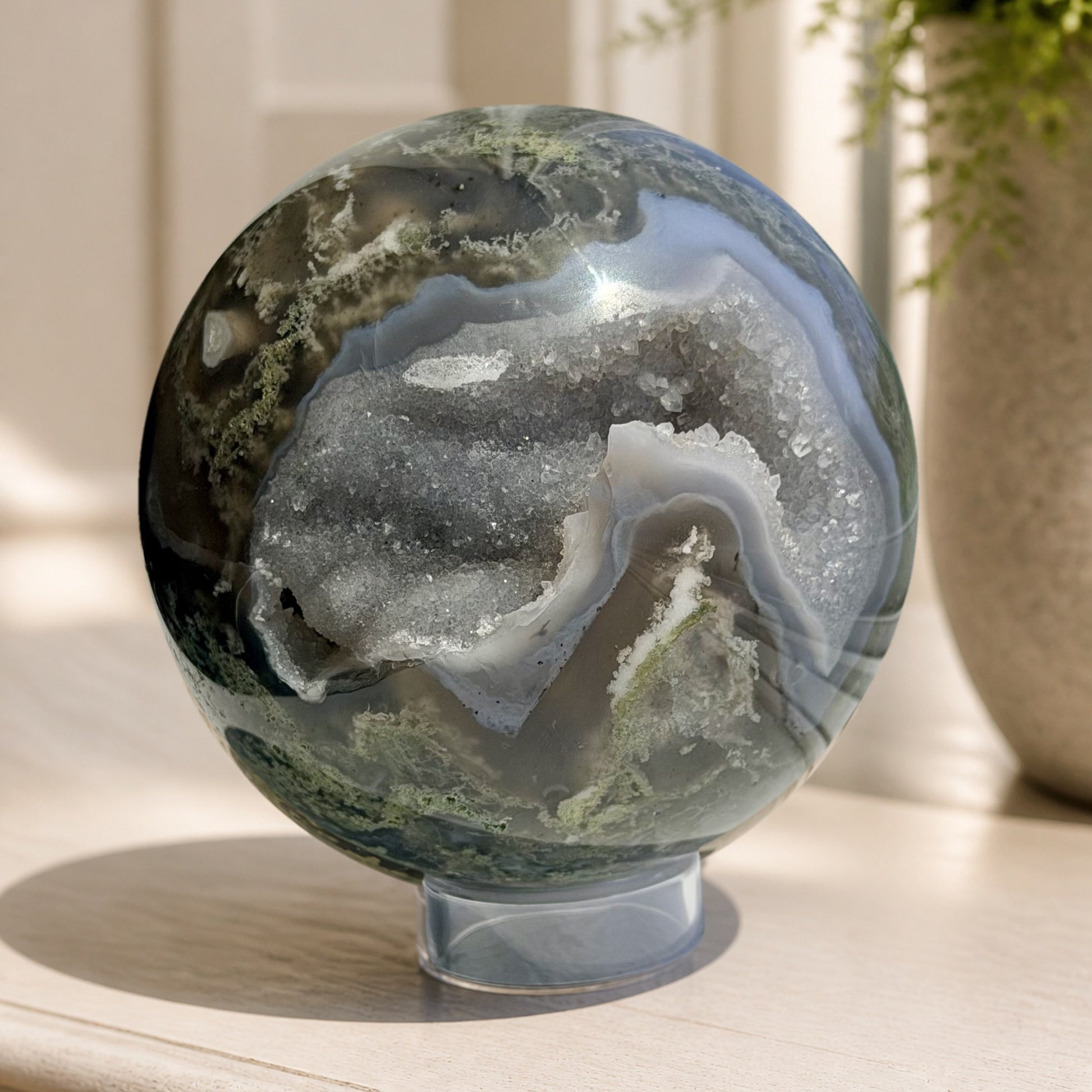 Moss agate sphere with druzy geode pocket displayed in a bright room