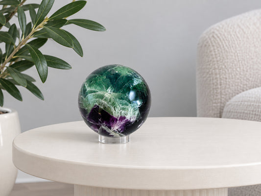 Rainbow fluorite sphere on its clear acrylic stand on a side table