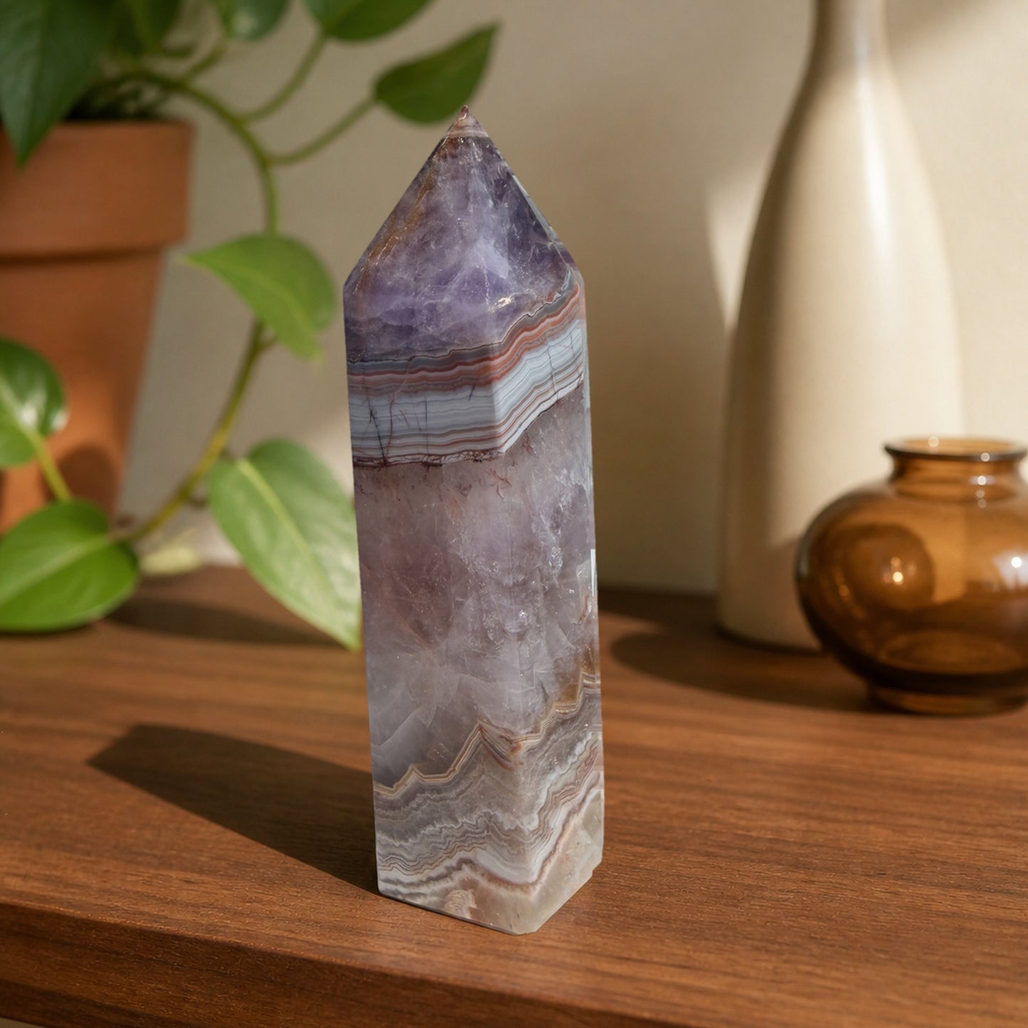 Amethyst crazy lace agate tower on a walnut shelf beside a trailing plant