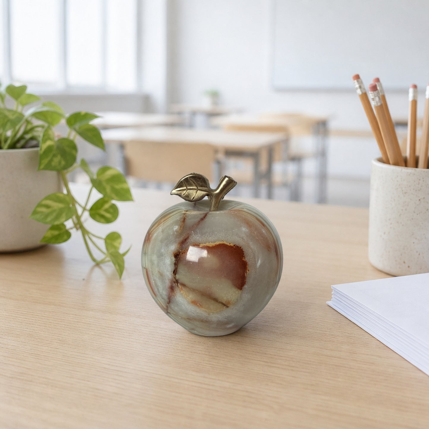 Carved onyx apple on a bright classroom desk with a plant and pencils