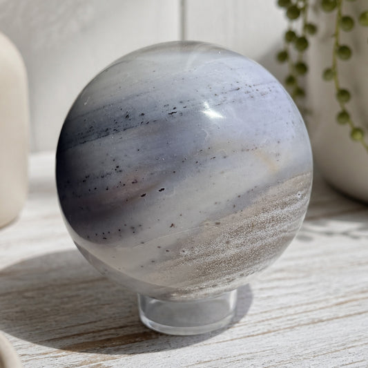 Blue and tan banded jasper sphere on a whitewashed wood surface with a string of pearls plant