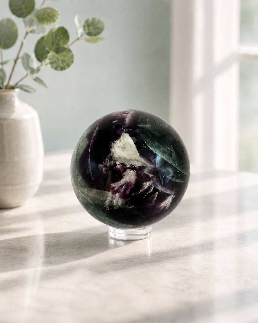Rainbow fluorite sphere lifestyle on marble counter with eucalyptus