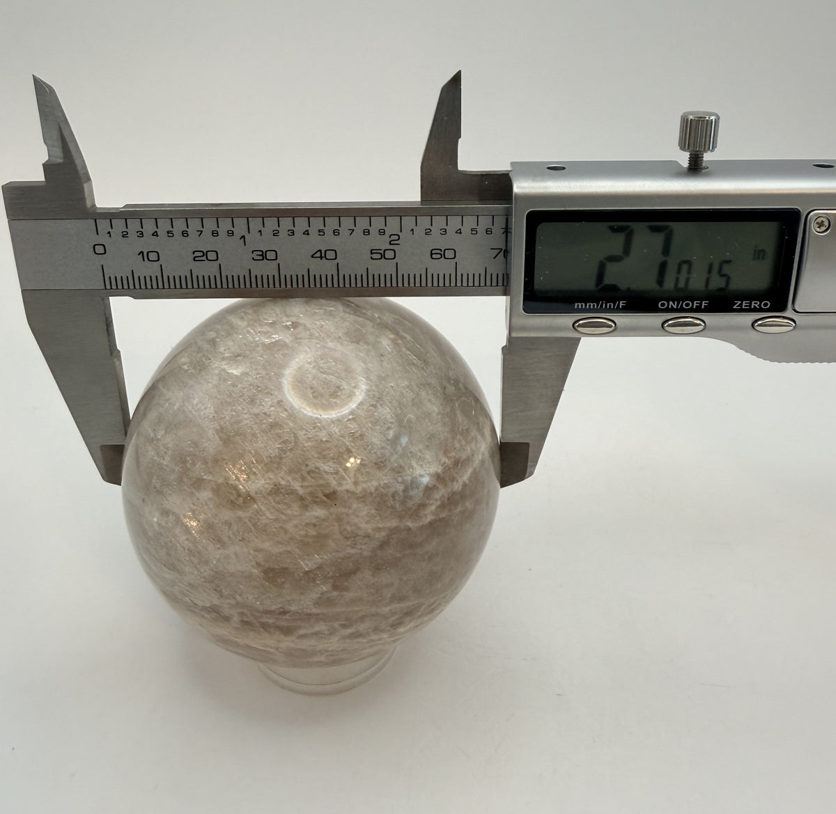 Peach moonstone sphere in a digital caliper reading 2.7 inches