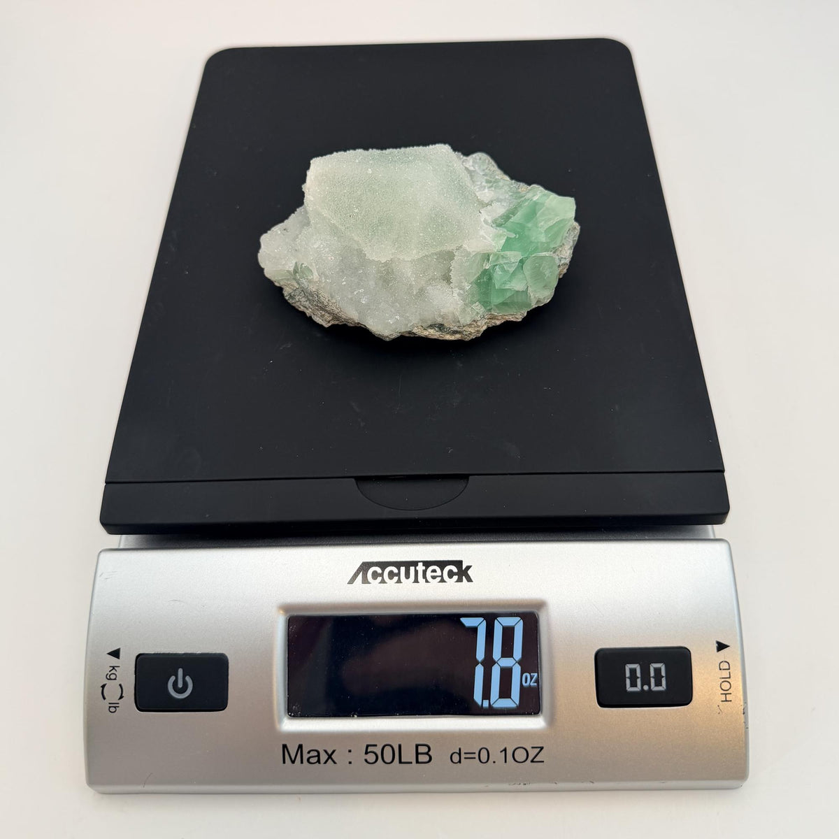 Green fluorite cluster with druzy quartz on a black display stand