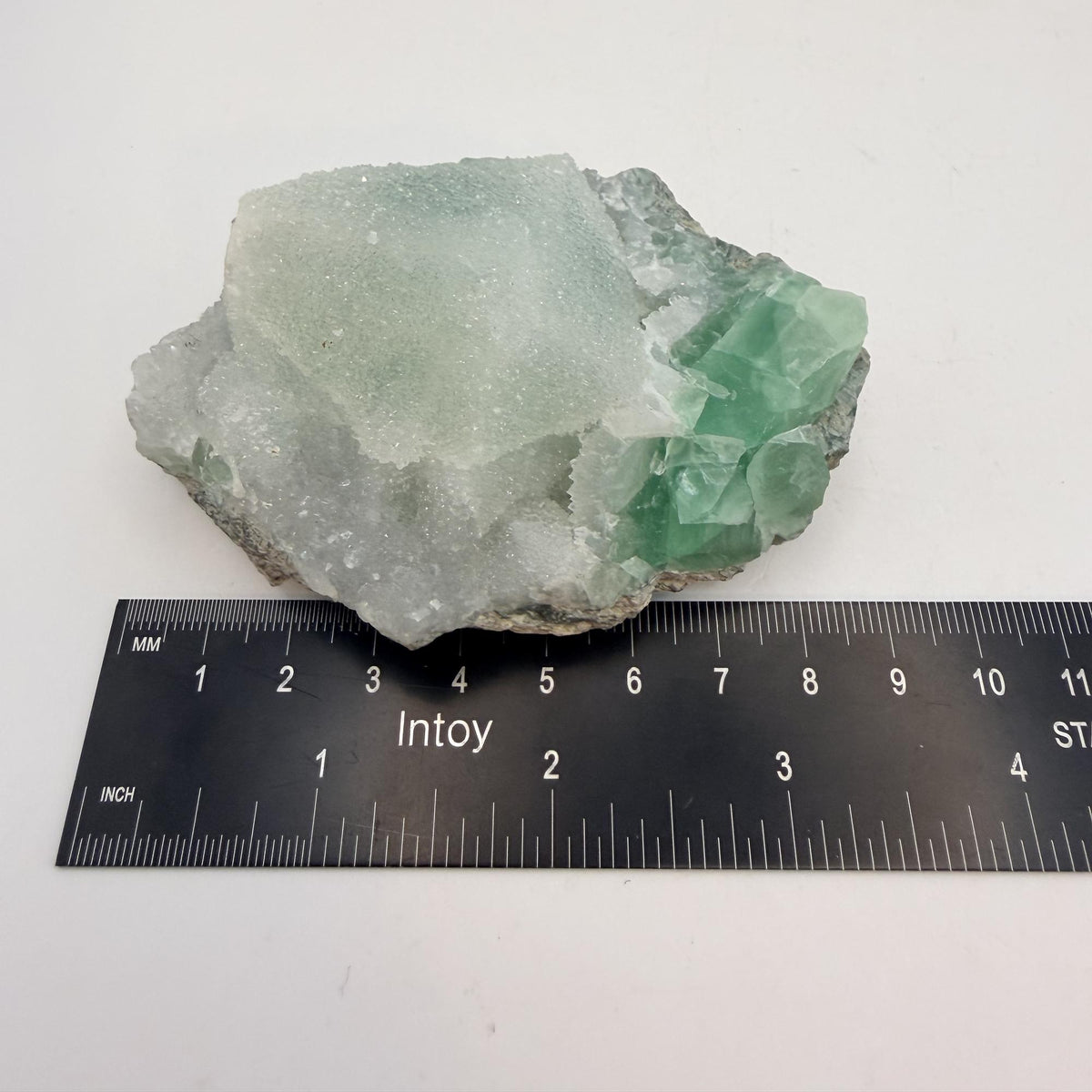 Green fluorite cluster with druzy quartz on a black display stand