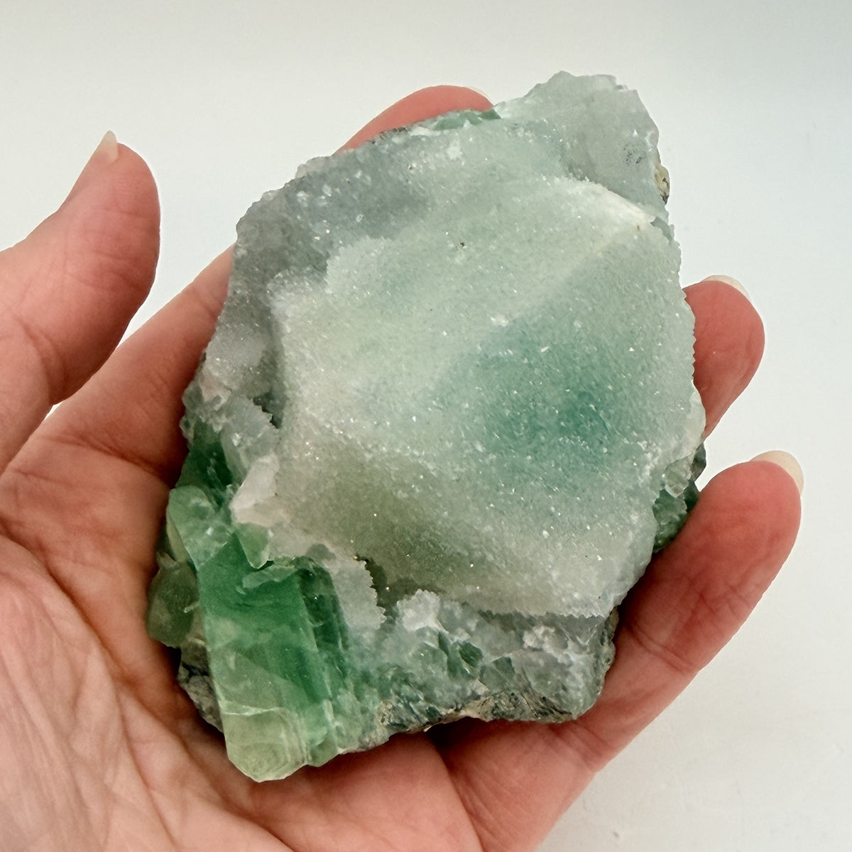Green fluorite cluster with druzy quartz on a black display stand