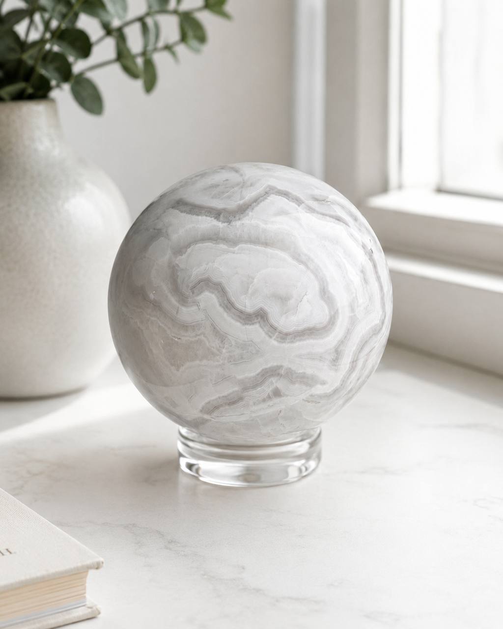 Grey banded onyx sphere on marble surface by window