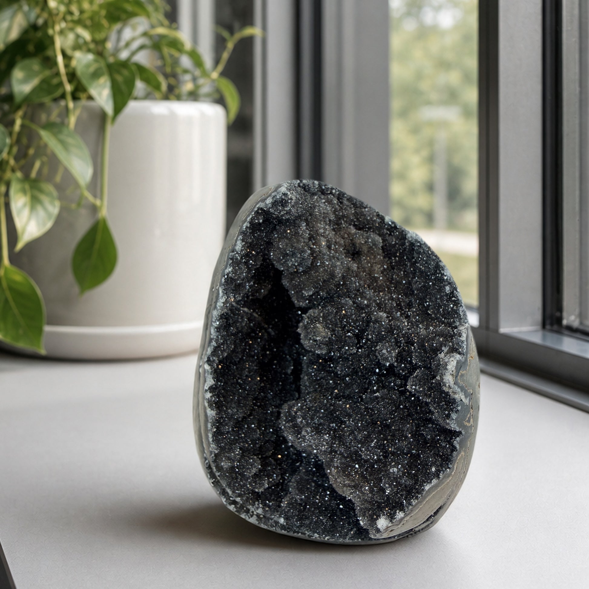 Black druzy quartz geode on a windowsill beside a pothos plant