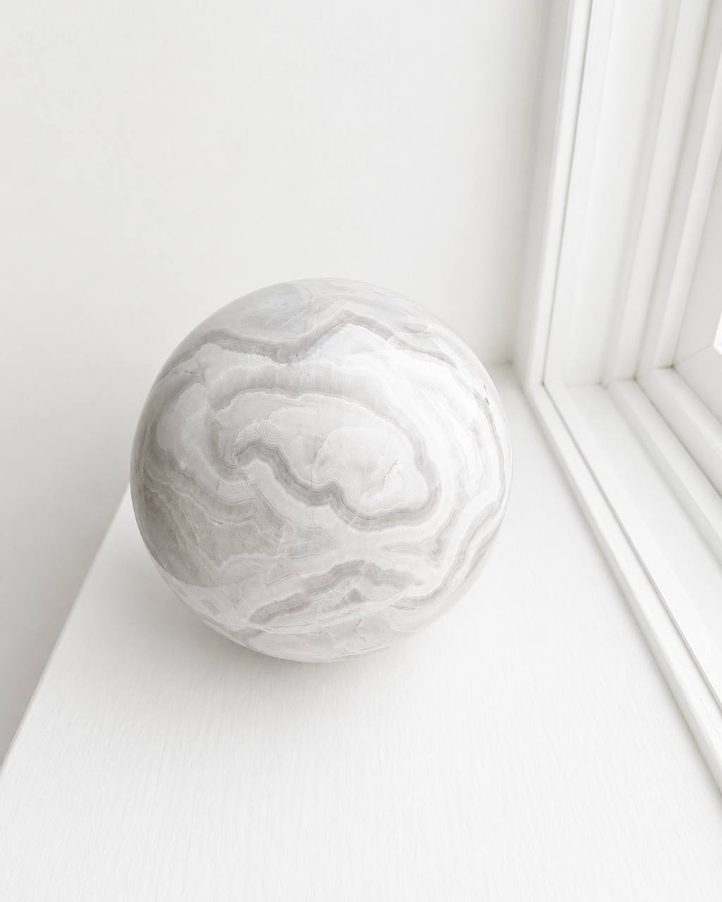 Grey banded onyx sphere on white windowsill